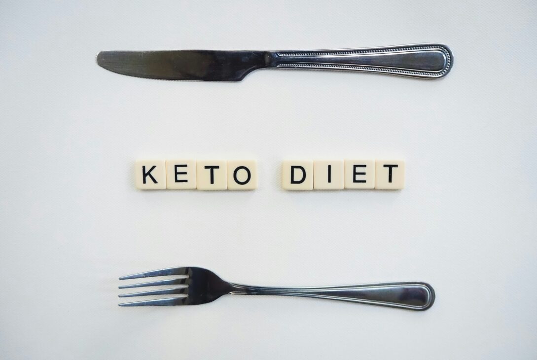 Research suggests that a ketogenic diet could improve the efficacy of prostate cancer treatment. In this image, the words KETO DIET are spelled out using Scrabble squares. A knife sits above the words and a fork sits below it.