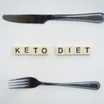 Research suggests that a ketogenic diet could improve the efficacy of prostate cancer treatment. In this image, the words KETO DIET are spelled out using Scrabble squares. A knife sits above the words and a fork sits below it.