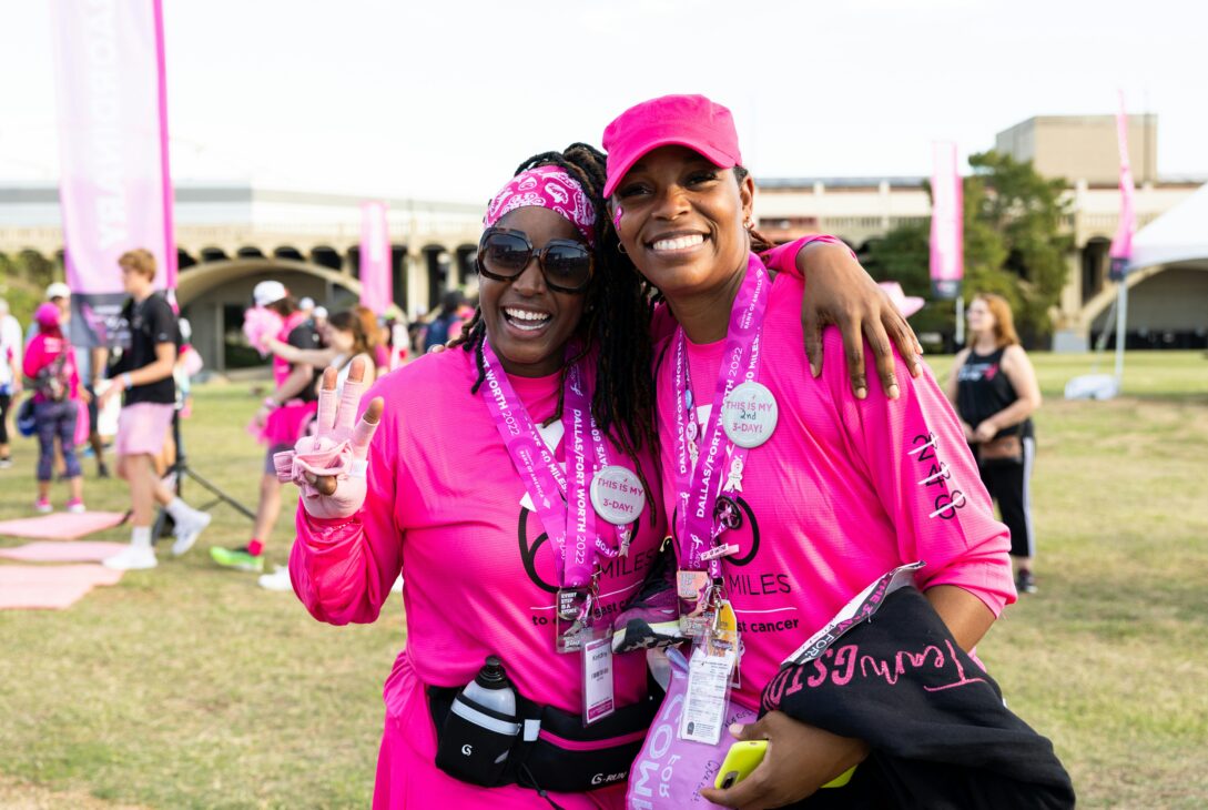 Two Black women stand at a Susan G. Komen rally for breast cancer awareness, including triple-negative breast cancer (TNBC). They are decked out in the bright pink associated with breast cancer awareness.