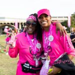 Two Black women stand at a Susan G. Komen rally for breast cancer awareness, including triple-negative breast cancer (TNBC). They are decked out in the bright pink associated with breast cancer awareness.